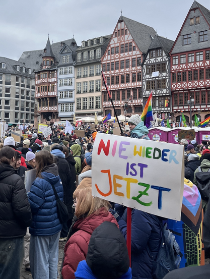 Schild mit „Nie wieder ist jetzt“-Slogan im Vordergrund.